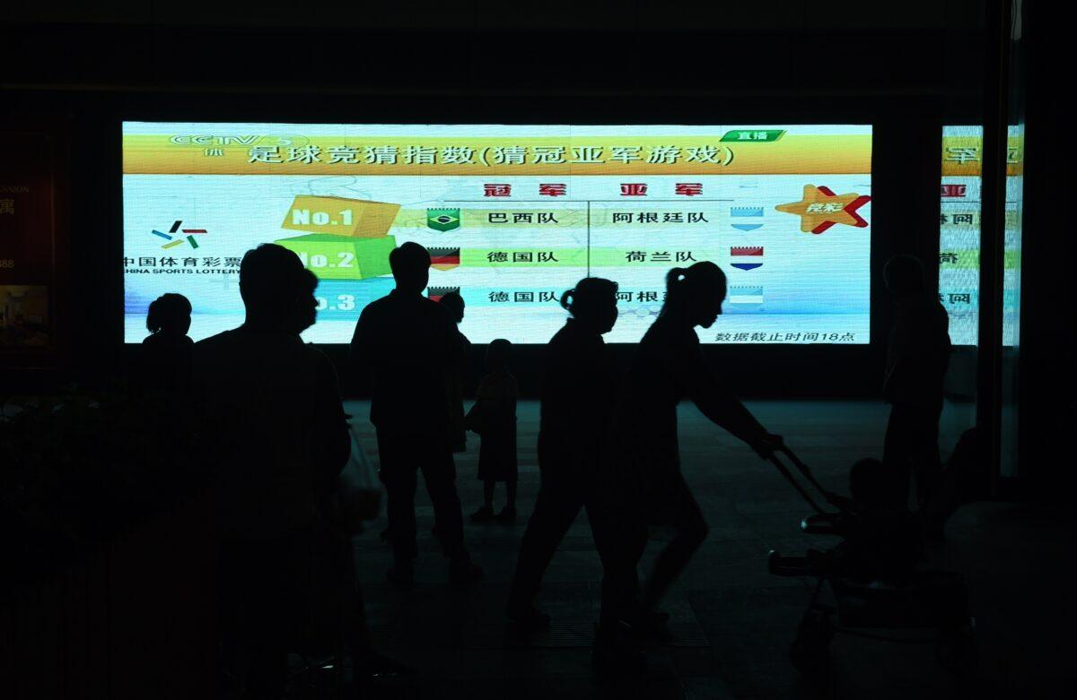 People walking past a TV screen showing a 2014 football World Cup-themed game sponsored by the China Sports Lottery, outside a shopping mall in Beijing, on June 30, 2014. (Greg Baker/AFP via Getty Images)