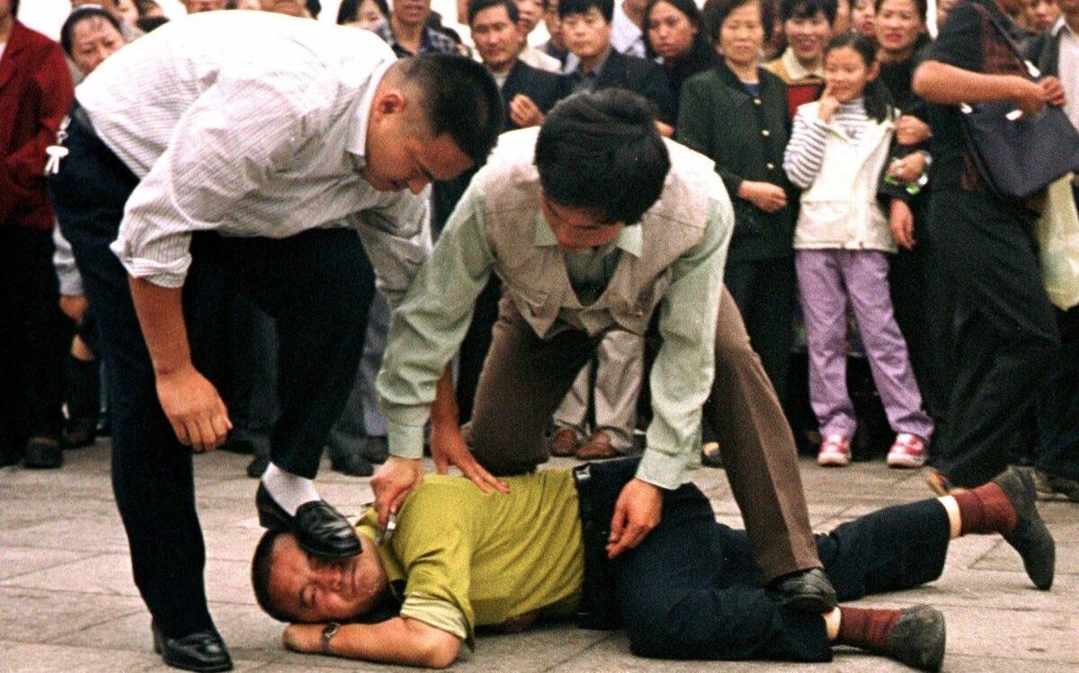 Police detain a Falun Gong practitioner in Tiananmen Square as a crowd watches in Beijing on Oct. 1, 2000. (Chien-min Chung/AP Photo)