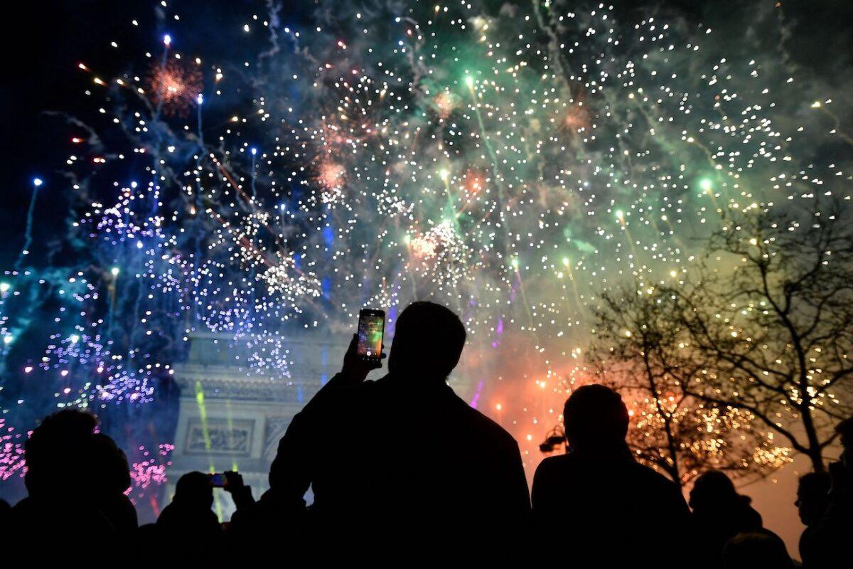 A spectator holds a smartphone as fireworks explode next to the Arc de Triomphe, at the Avenue des Champs-Elysees during New Year celebrations in Paris, early on Jan. 1, 2023. (Julien de Rosa/AFP via Getty Images)