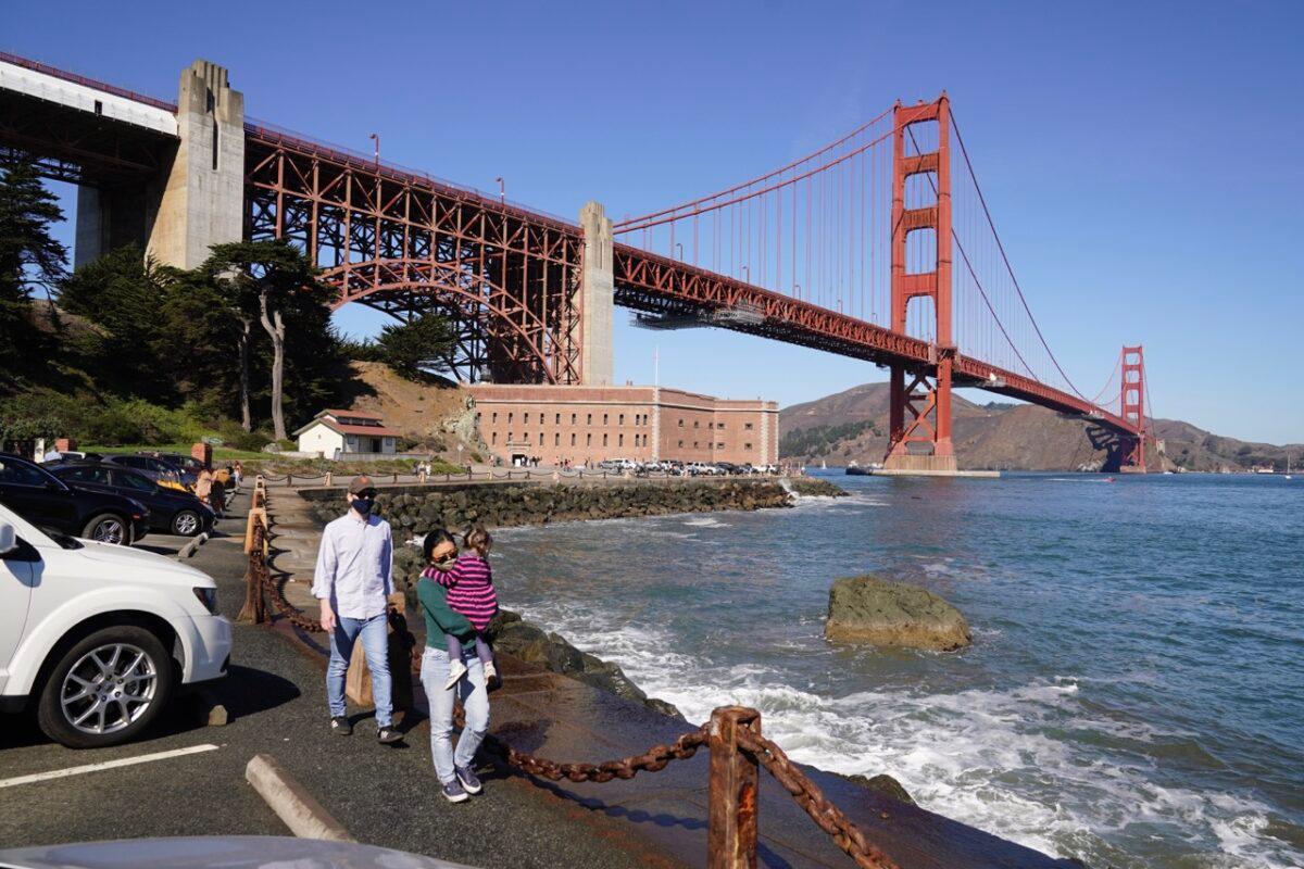 People walk along a seawall with Fort Point and the Golden Gate Bridge in the background in San Francisco, on Oct. 11, 2020. (Eric Risberg/AP Photo)