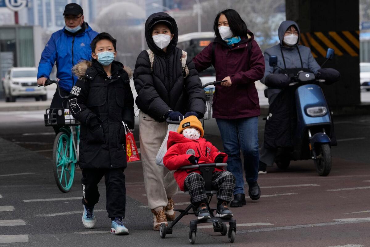 A child wearing a mask is pushed across a road in Beijing on Dec. 2, 2022. (Ng Han Guan/AP Photo)