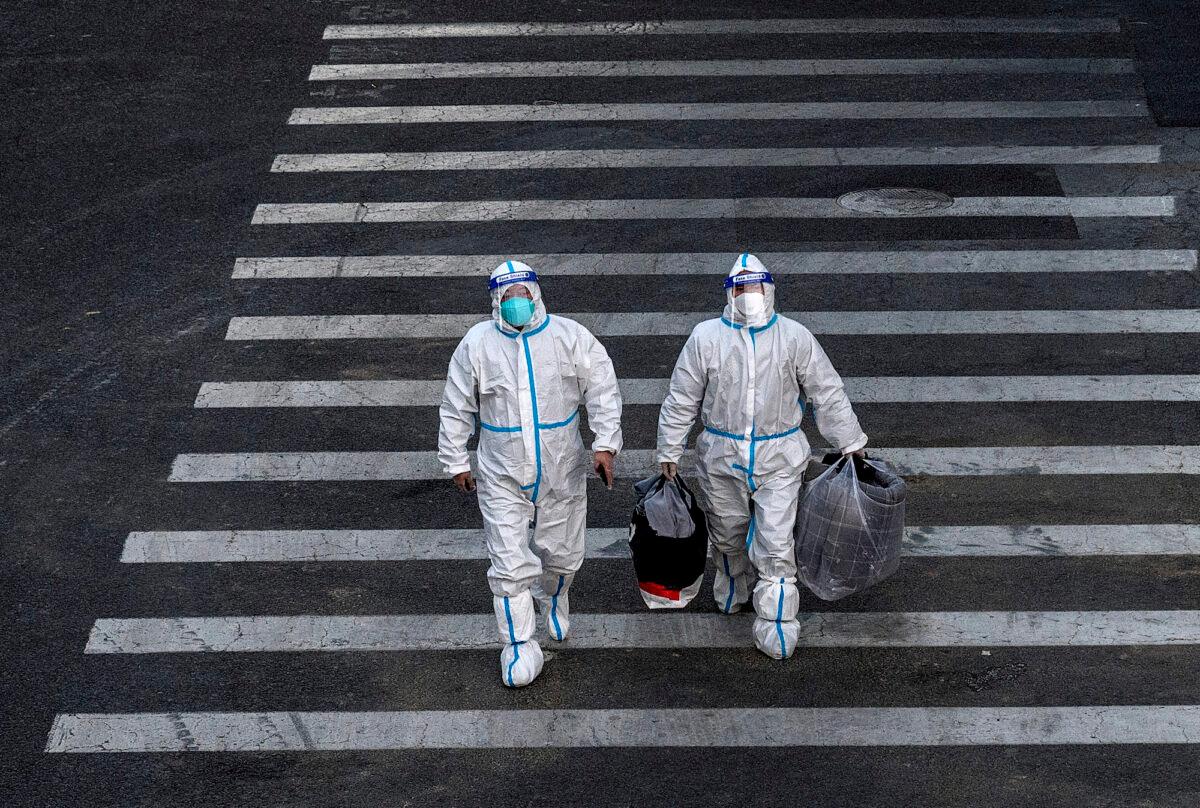 Epidemic control workers wear PPE to prevent the spread of COVID-19 as they walk across a road on their way to perform nucleic acid tests in an area with communities in lockdown in Beijing, on Dec. 1, 2022. (Kevin Frayer/Getty Images)