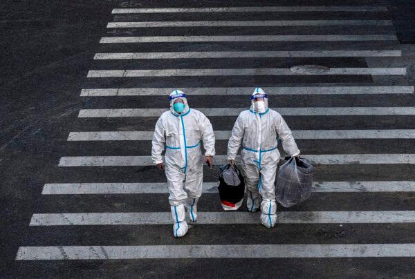 Epidemic control workers in PPE walk across a road on their way to perform nucleic acid tests in an area with communities in lockdown in Beijing, China, on Dec. 1, 2022. (Kevin Frayer/Getty Images)