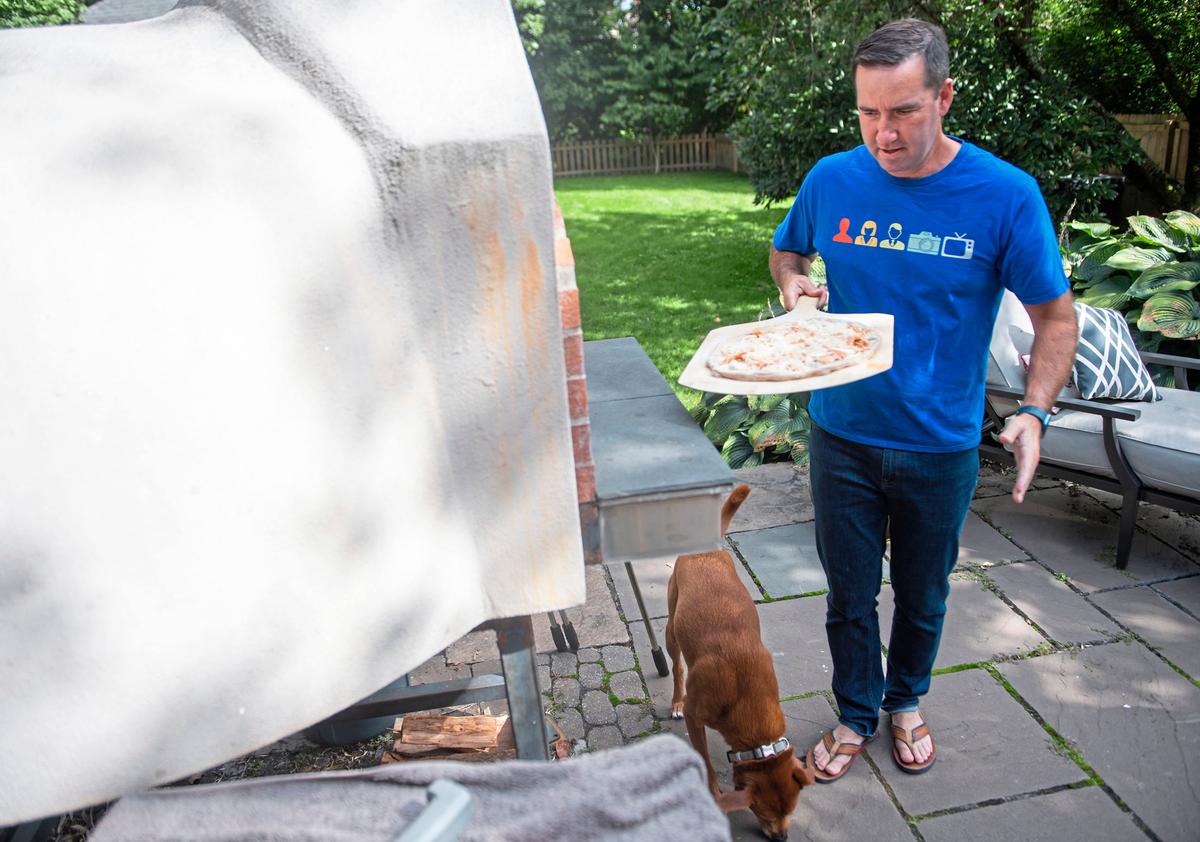 Chris Hayes prepares to put a buffalo chicken pizza in his pizza oven while his dog Charlie looks for any fallen toppings in Ben Avon, Pa., on Sept. 24, 2022. (Emily Matthews/Pittsburgh Post-Gazette/TNS)