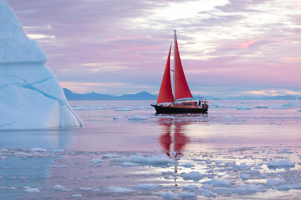 A small red sailboat cruises among icebergs from Disko Bay glacier, Greenland. (Kertu/Shutterstock)