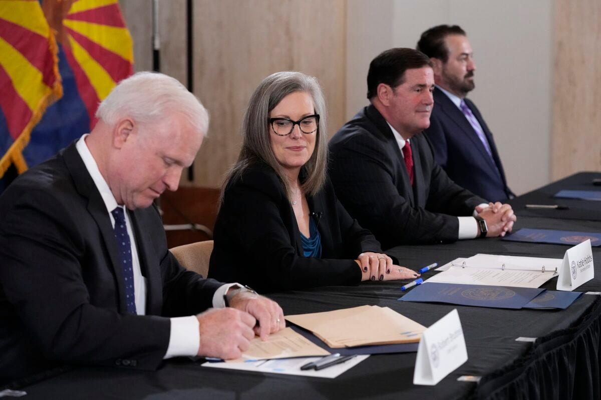 Arizona Supreme Court Chief Justice Robert Brutinel (L) signs the official Arizona general election canvass document as Katie Hobbs, the Democratic governor-elect and current secretary of state (2nd L) looks on, while Arizona Republican Gov. Doug Ducey (2nd R) and Arizona Attorney General Mark Brnovich (R) sit at the table as well during a signing ceremony at the Arizona Capitol in Phoenix on Dec. 5, 2022. (Ross D. Franklin/Pool/AP Photo)