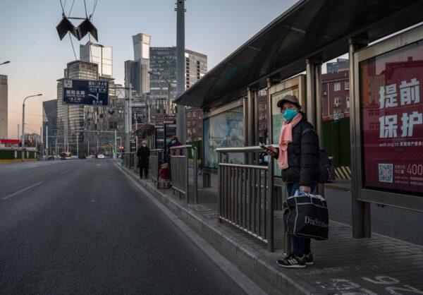 A woman wears a mask to protect against the spread of COVID-19 as she waits at a bus stop on a usually busy street in the Central Business District in Beijing on Dec. 6, 2022. In recent weeks, China has been recording some of its highest numbers of COVID-19 cases since the pandemic began. (Kevin Frayer/Getty Images)