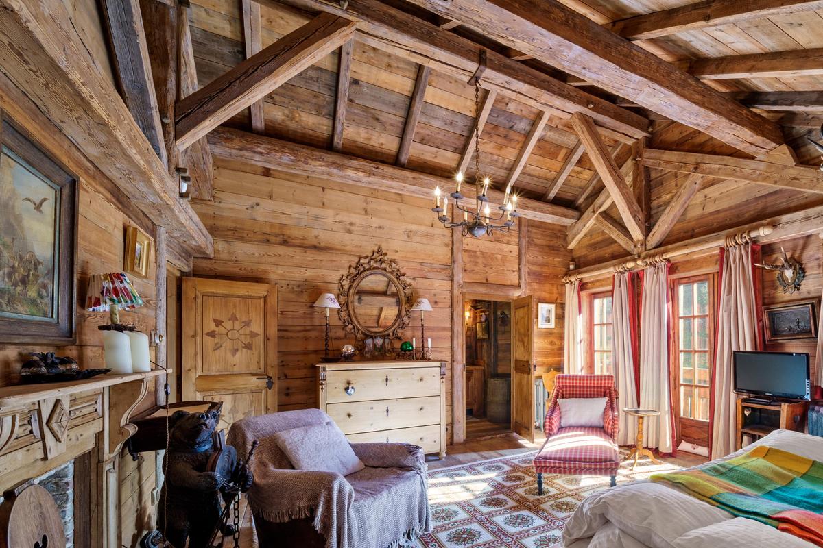 This spacious bedroom features an exposed beam ceiling and a fireplace, as well as rustic wood floors, a chandelier, and access to the balcony to enjoy the view. (Courtesy of Sotheby’s Concierge Auctions)