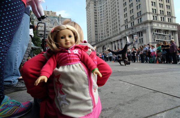 A girl with her doll peeking out of her backpack watches as a street entertainer dances during a road side show on Oct. 9, 2015 in New York. (Jewel Samad/AFP via Getty Images)