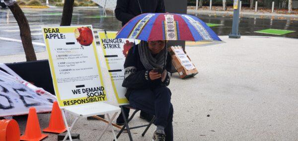 Han Wang sits under an umbrella outside Apple’s headquarters on Dec. 10, 2022. (David Lam/NTD)