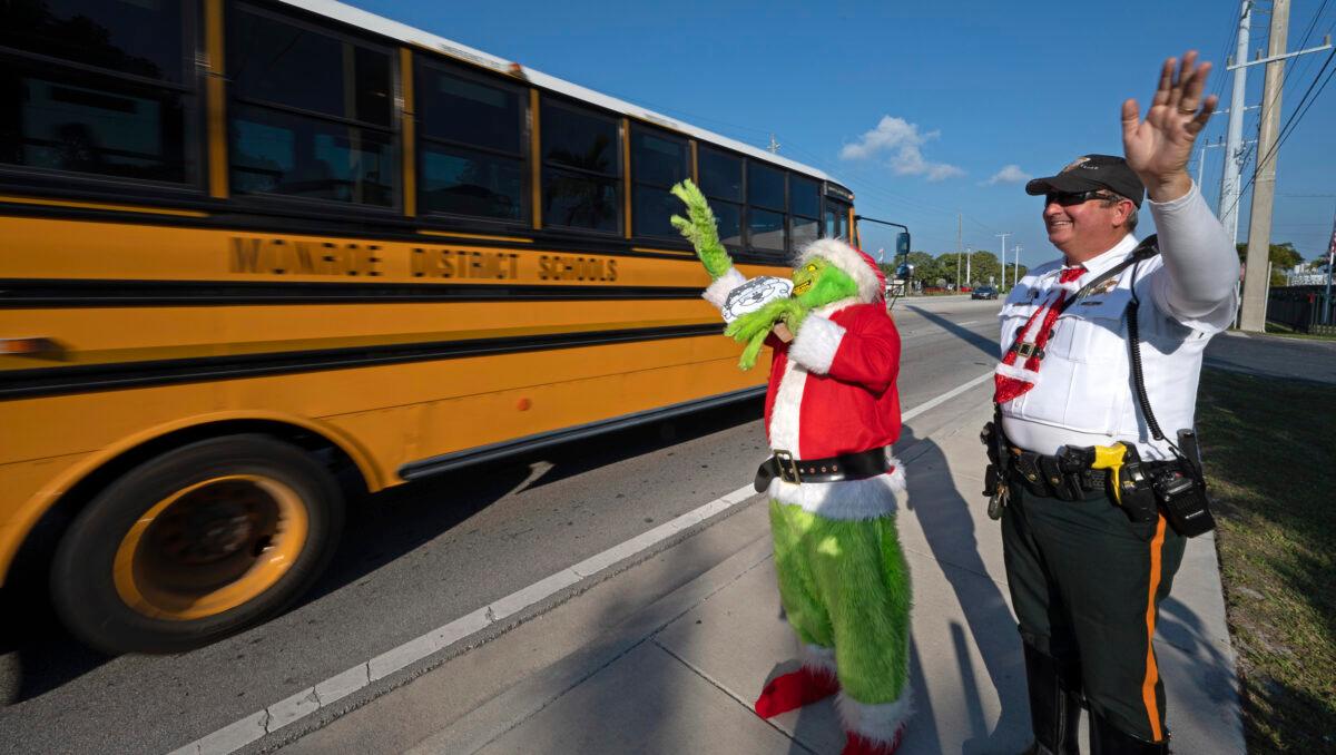 Monroe County Sheriff's Office Colonel Lou Caputo, (L), costumed as the Grinch, and Deputy Andrew Leird (R) wave at a school bus rolling on the Florida Keys Overseas Highway in Marathon, Fla., on Dec. 13, 2022. (Andy Newman/Florida Keys News Bureau via AP)
