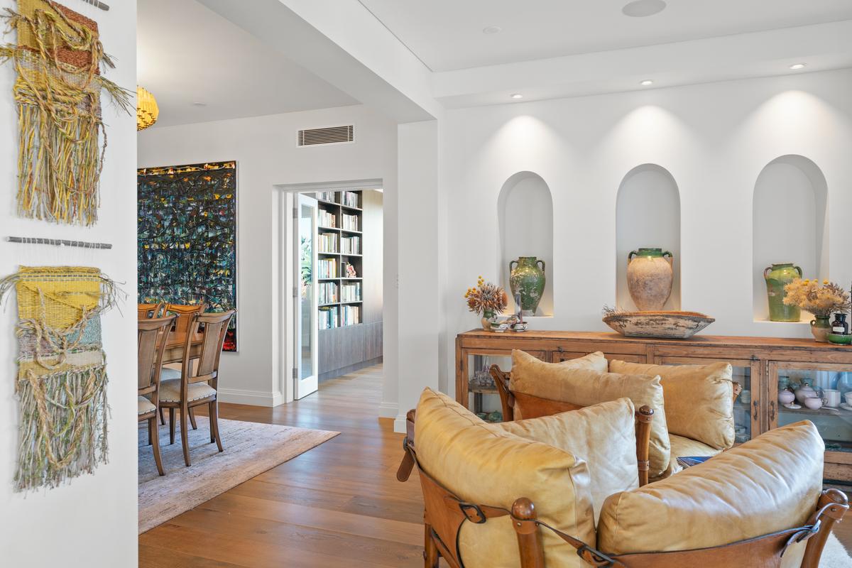 Throughout the residence, the rooms are airy , with warm wood floors as seen in the living room adjacent the dining area, and a den beyond. (Sydney Sotheby’s International Realty)
