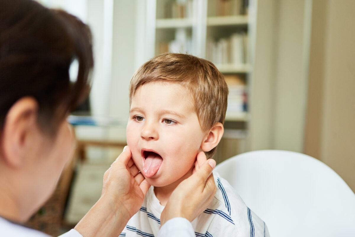 A pediatrician feels the tonsils in a child with a sore throat and shows his tongue. (Shutterstock)