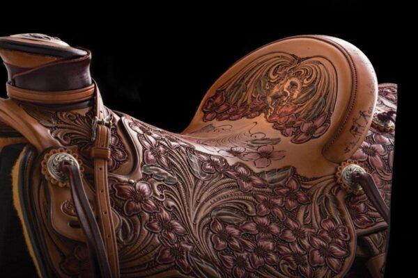 A close-up detail of Cary Schwarz's 3/4 saddle shows a sea of syringa flowers, and on the saddle dish a rider attempts to tame his bucking bronco. (National Cowboy & Western Heritage Museum)