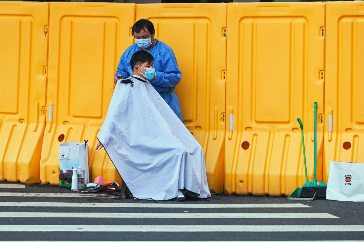 A man receives a haircut on a street adjoining a neighborhood that authorities locked down over fears of the COVID-19 pandemic in the Jing'an district of Shanghai, on May 30, 2022. (HECTOR RETAMAL/AFP via Getty Images)