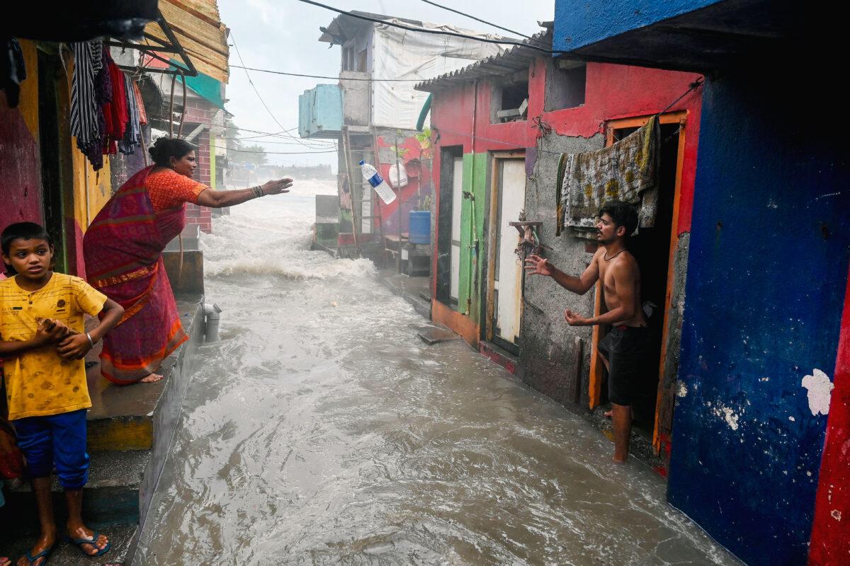 A woman throws a bottle of drinking water to her neighbor as sea water gushes into a residential area near the seafront at high tide during monsoon season in Mumbai, India, on June 15, 2022. (INDRANIL MUKHERJEE/AFP via Getty Images)