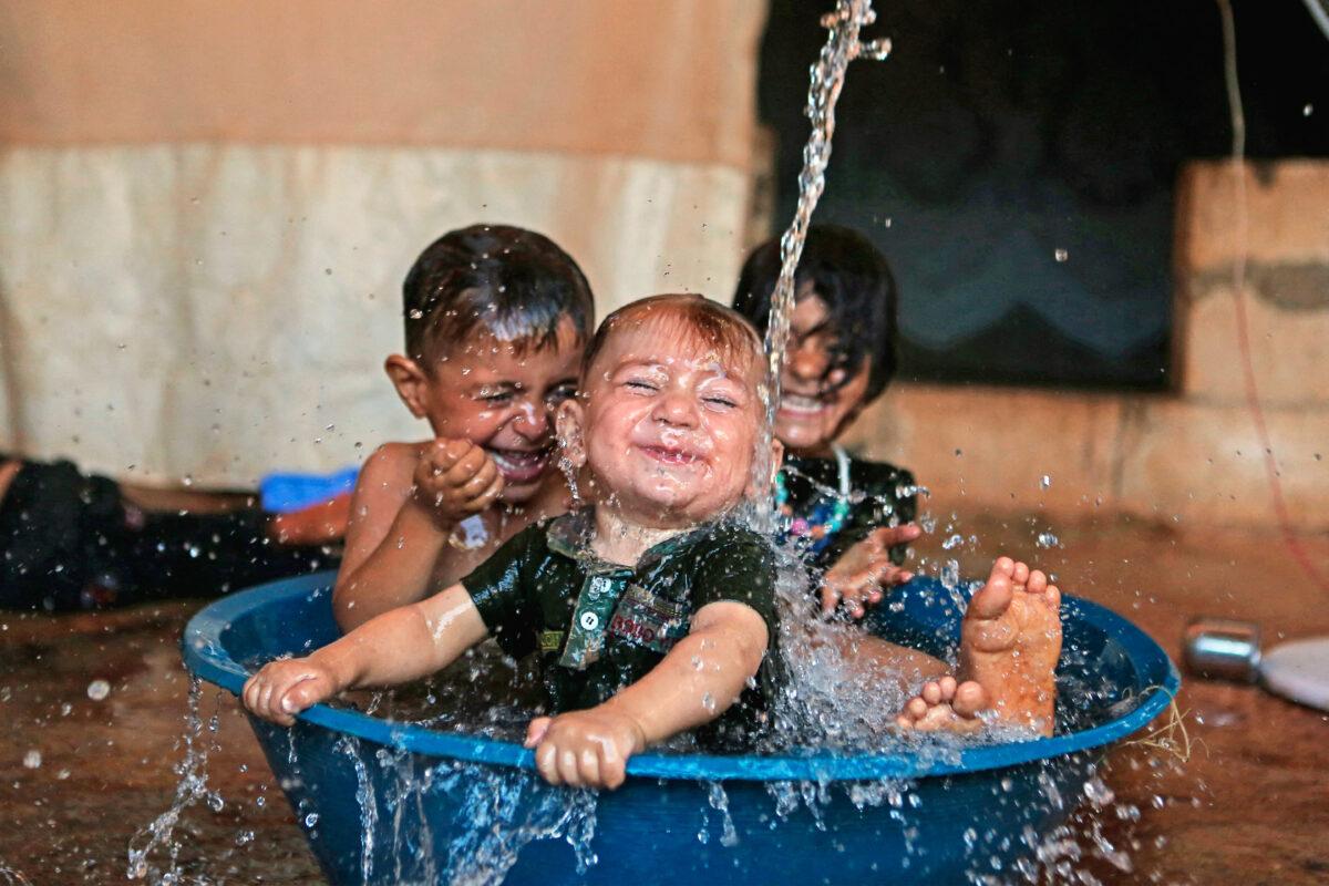 Children play in a water-filled wash tub amid soaring temperatures in a camp for the internally displaced, near the Syrian village of Killi in the rebel-held northwestern province of Idlib, on July 31, 2022. (AAREF WATAD/AFP via Getty Images)