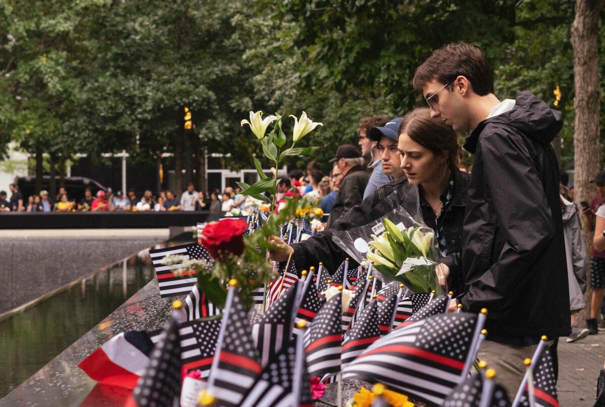 People place flags and flowers next to the names of those who died in the 2001 attacks, at the World Trade Center Memorial in New York on Sept. 11, 2022. (Chung I Ho/The Epoch Times)