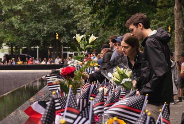 People place flags and flowers next to the names of those who died in the 2001 attacks, at the Sept. 11 memorial in New York on Sept. 11, 2022. (Chung I Ho/The Epoch Times)