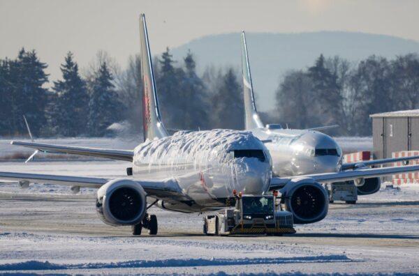 An Air Canada aircraft covered with snow and ice is moved by a tug as a Westjet aircraft is seen being moved behind it, at Vancouver International Airport in Richmond, B.C., on Dec. 21, 2022. (Darryl Dyck/The Canadian Press)
