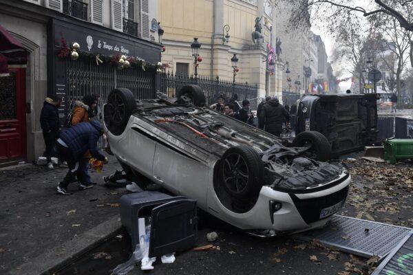 People pass by cars that have been turned over during clashes following a demonstration of members of the Kurdish community at The Place de la Republique in Paris on Dec. 24, 2022. (Julien de Rosa/AFP via Getty Images)