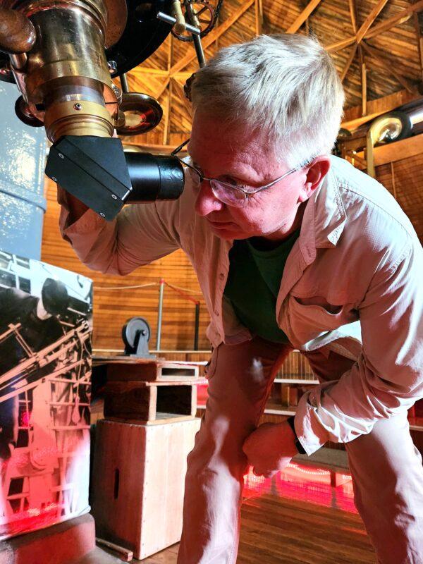 Lowell Observatory historian Kevin Schindler peers through the eyepiece of the 24-inch refractor telescope in Flagstaff, Ariz., on Dec. 20, 2022. The telescope has the fifth-largest refractor in the world and is still used in planetary research. (Allan Stein/The Epoch Times)