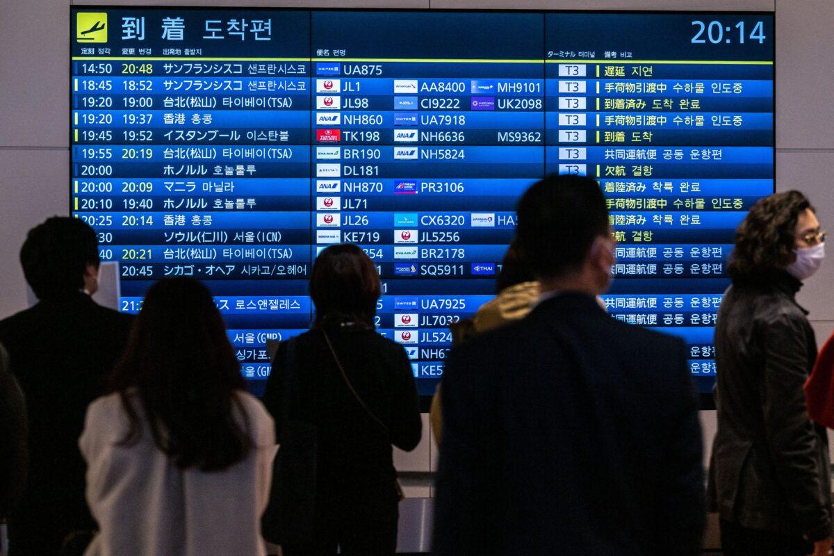 People wait in front of a board showing international flight arrivals at Tokyo's Haneda international airport on Dec. 28, 2022. (Philip Fong/AFP via Getty Images)