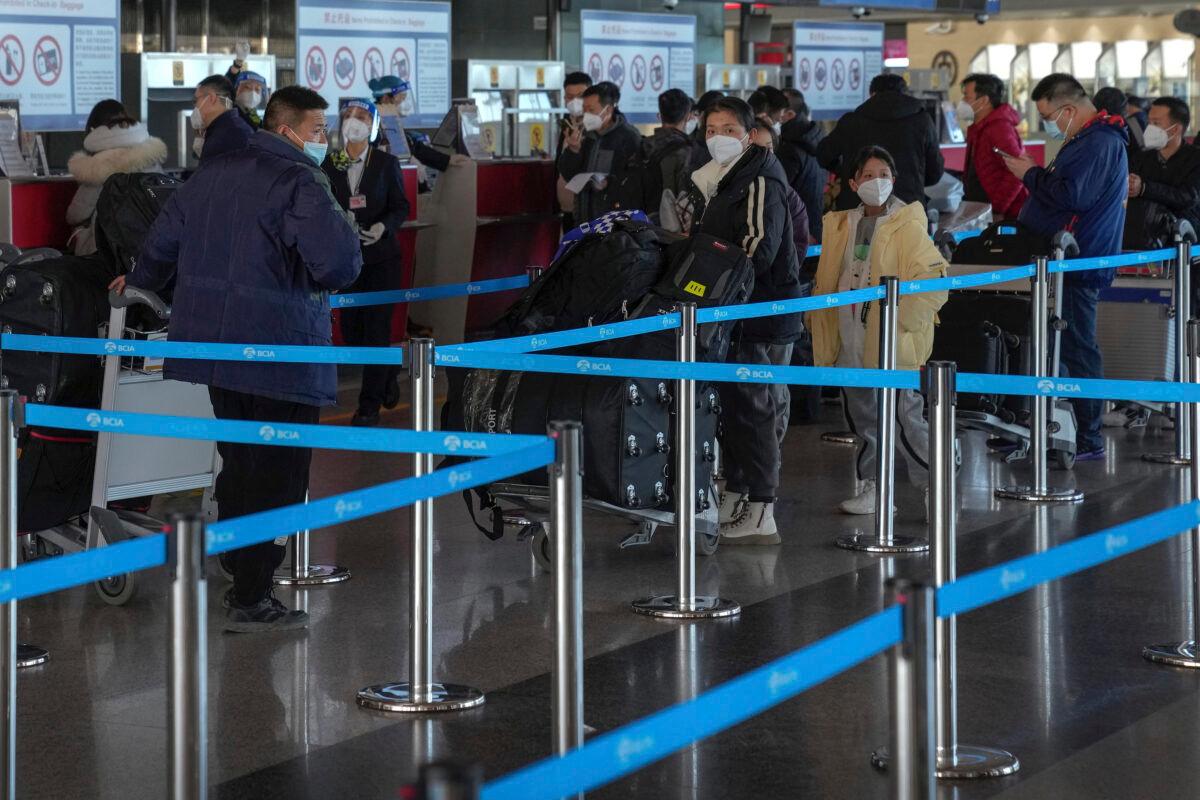 Masked travelers with luggage line up at the international flight check in counter at the Beijing Capital International Airport in Beijing, on Dec. 29, 2022. (Andy Wong/AP Photo)