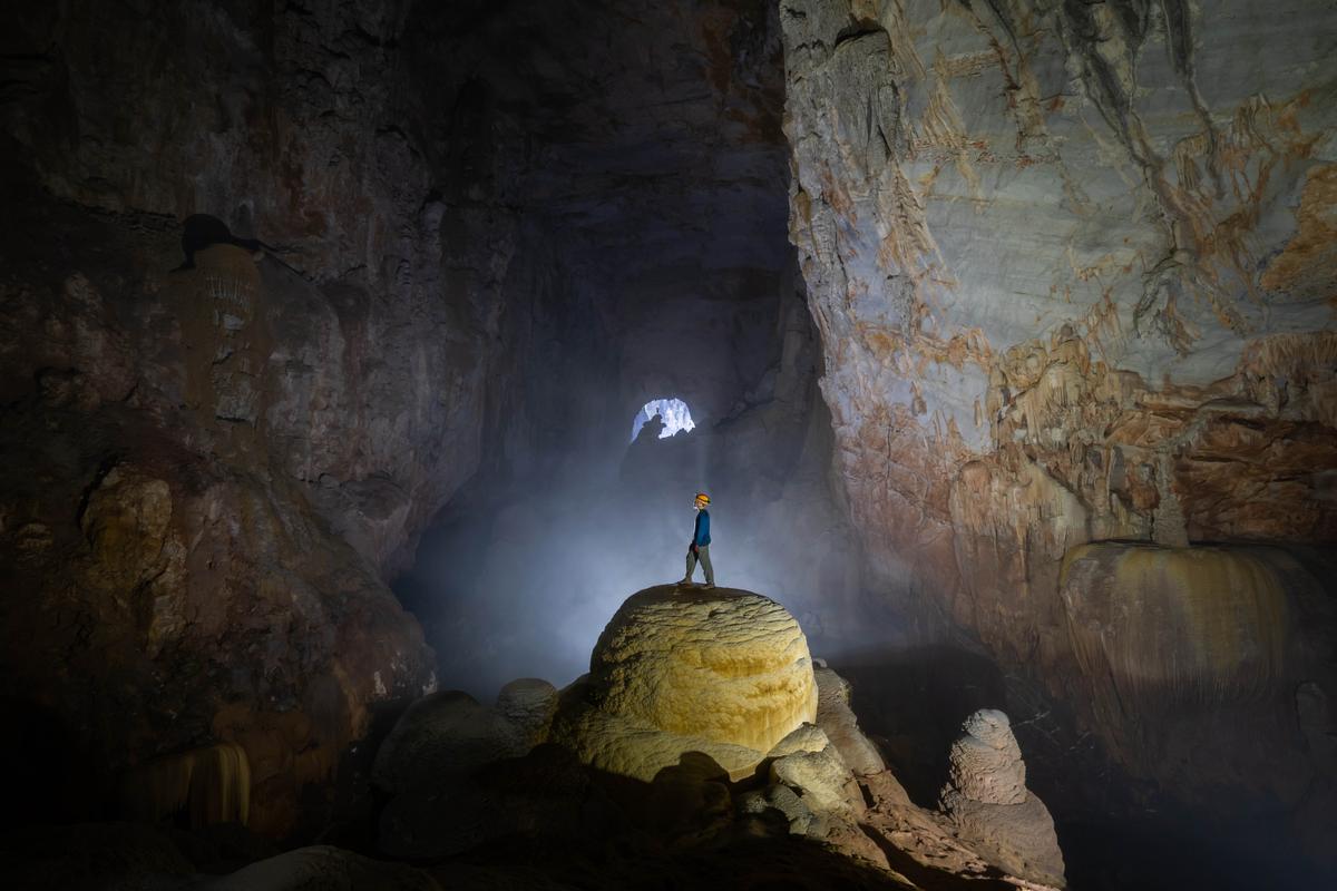 A cave explorer stands atop a massive stalagmite in the cave. (kid315/Shutterstock)