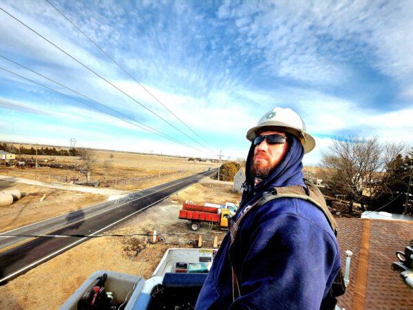 Dylon Braun, a Midwest Energy power line worker, surveys the wires on a nearby utility pole from atop a company bucket truck in Ellis County, Kansas, on Jan. 4, 2023. (Allan Stein/The Epoch Times)