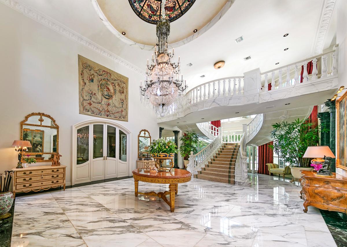 The entry foyer features a spectacular chandelier, gleaming marble flooring, and a sweeping staircase leading to the upper level. (Courtesy of Jade Mills Estates)