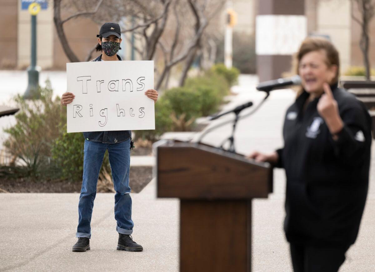 A transgender-rights activist holds a sign while Idaho state Rep. Barbara Erhardt (R) speaks during a rally outside of the NCAA Convention in San Antonio, Texas, on Jan. 12, 2023. (Darren Abate/AP Photo)