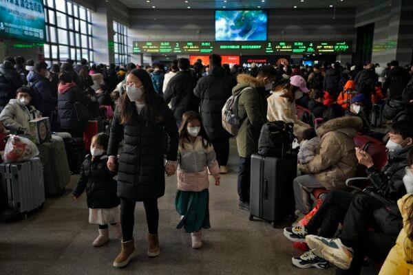 A woman and children wearing face masks walk by masked travelers waiting at a departure hall to catch their trains at the West Railway Station in Beijing on Jan. 15, 2023. (Andy Wong/AP Photo)