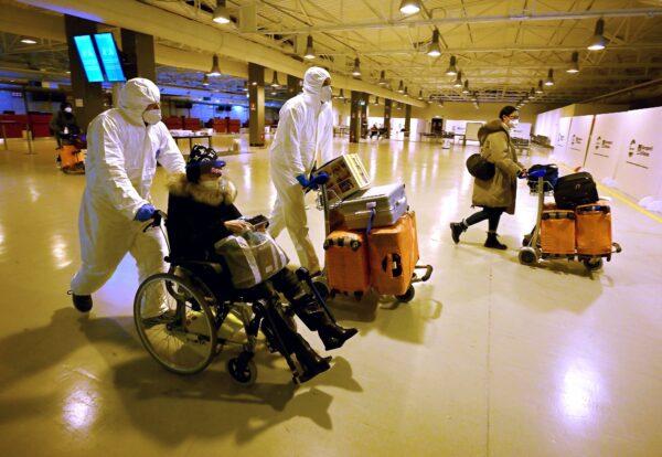 Workers wearing protective masks and suits help Chinese travelers leaving the arrival hall after being tested for the COVID-19 virus at Rome Fiumicino International Airport, near Rome, on Dec. 29, 2022. (Filippo Monteforte/AFP via Getty Images)