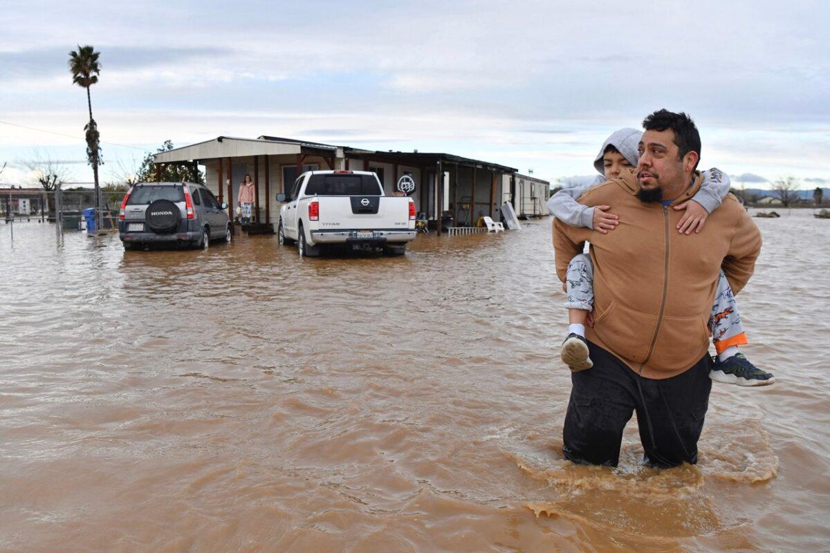 A man carries his son on his back while his wife waits at the front porch to be rescued from their flooded home in Brentwood, Calif., on Jan. 16, 2023. (Jose Carlos Fajardo/Bay Area News Group via AP)