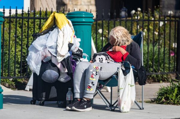 A homeless woman sits along Harbor Boulevard, in Anaheim, Calif., on Jan. 18, 2023. (John Fredricks/The Epoch Times)