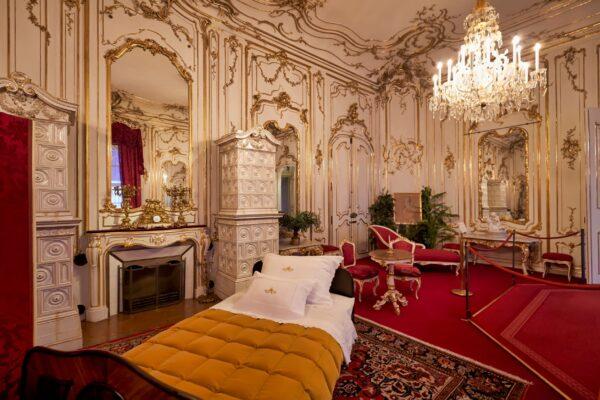 Here we have an unusual room in the Imperial apartments. While it may at first look like a typical baroque room with its ornate mirrors, crystal chandelier, and gilded walls and ceiling, some elements are surprising. These are the simple wooden bed and the neo-Gothic family altar by Vinzenz Pilz near the fireplace. (Marcobrivio.photo/Shutterstock)