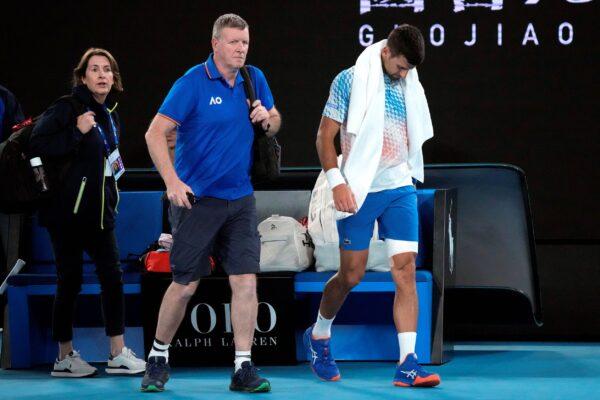 Novak Djokovic (R) of Serbia leaves the court with a trainer for an injury time out during his second round match against Enzo Couacaud of France at the Australian Open tennis championship in Melbourne, Australia, on Jan. 19, 2023. (Dita Alangkara/AP Photo)