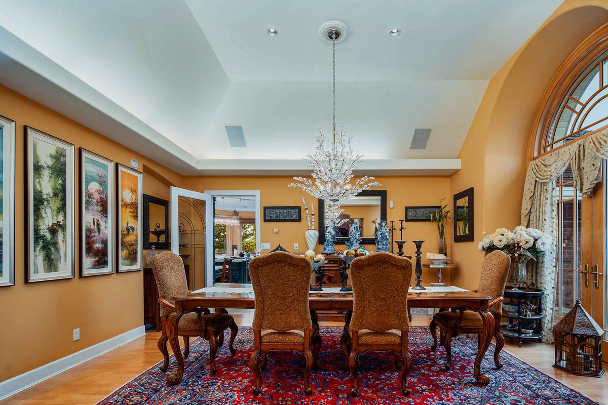 Adjacent to the kitchen, the formal dining room features a vaulted ceiling, a splendid crystal chandelier, and a great view of the surrounding grounds via the large windows with custom millwork. (Courtesy of Sotheby’s International Realty Canada)