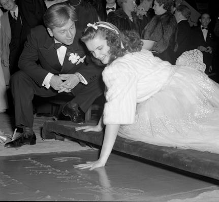 Mickey Rooney watching Judy Garland put handprint in cement at Grauman's Theatre during the "Babes in Arms" film premiere, 1939. (Public Domain)