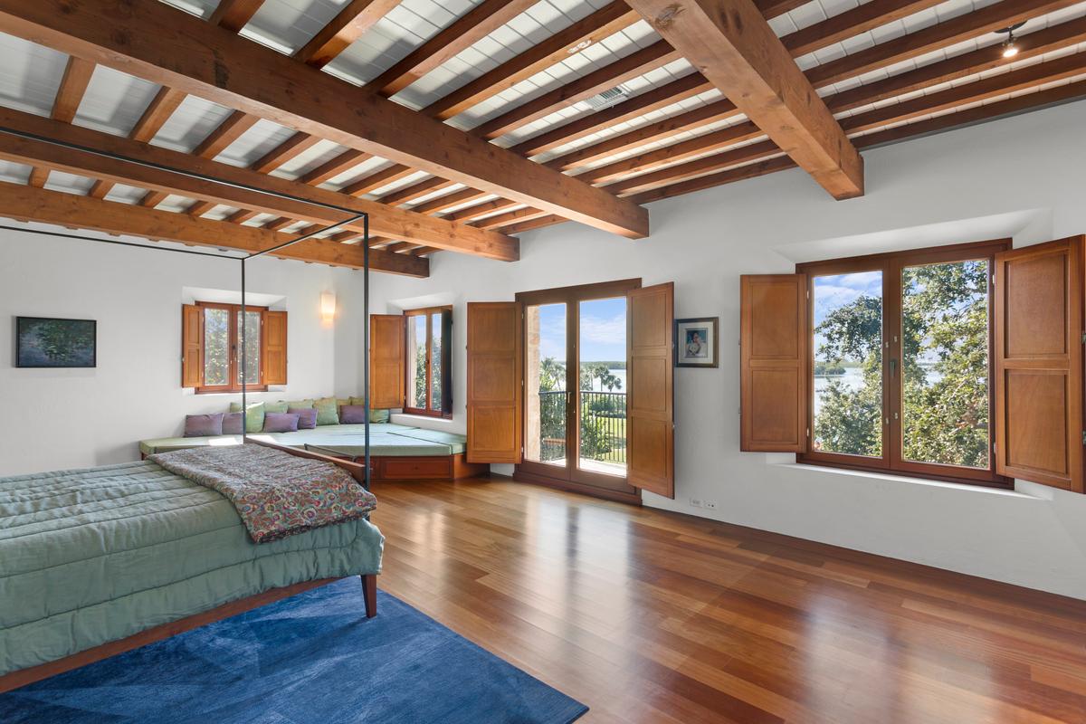 The expansive and airy master suite is a tranquil retreat, with exposed beam ceiling, wood flooring, a lounging area, and a clear view of the beautiful surroundings. (Courtesy of Sica Media)