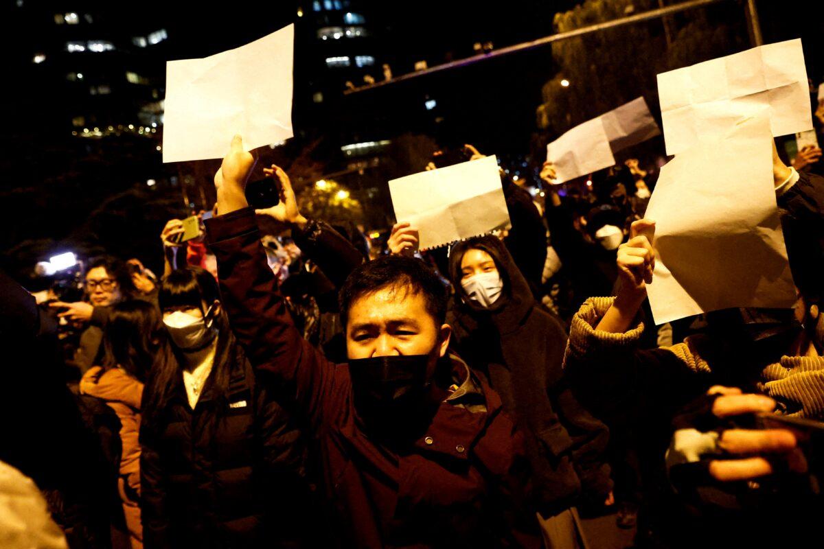 People gather for a vigil and hold white sheets of paper in protest of COVID-19 restrictions as they commemorate the victims of a fire in Urumqi, as outbreaks of the disease continue in Beijing, on Nov. 27, 2022. (Thomas Peter/Reuters)