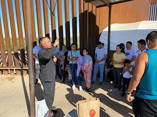 A Catholic priest blesses a group of newly arrived illegal migrants at the border wall in San Luis, Ariz. (Courtesy of San Luis Police Lt. Marco Santana)