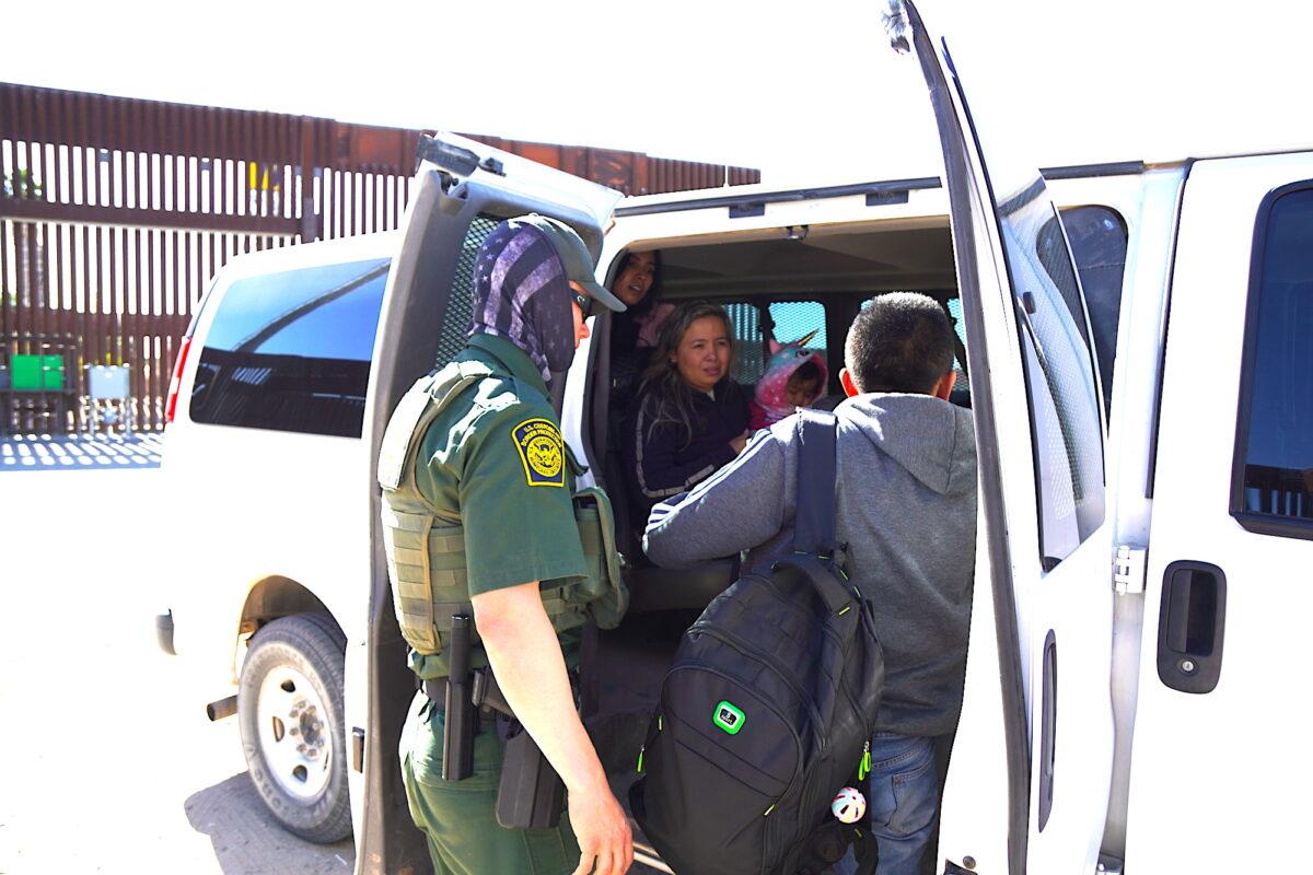 A U.S. Customs and Border Patrol agent loads a family of three from Columbia into a vehicle for transport to a federal processing facility on Jan. 27, 2023. (Allan Stein/The Epoch Times)