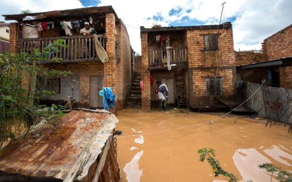 A man holding a child on his back stands on a doorstep flooded with rainwater in Antananarivo, Madagascar, on Jan. 28, 2023. (Alexander Joe/AP Photo)