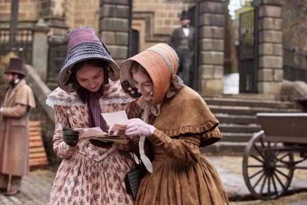 Charlotte (Alexandra Dowling, L) and her sister Anne (Amelia Gething) Brontë pour over reading material, in “Emily.” (Warner Bros.)