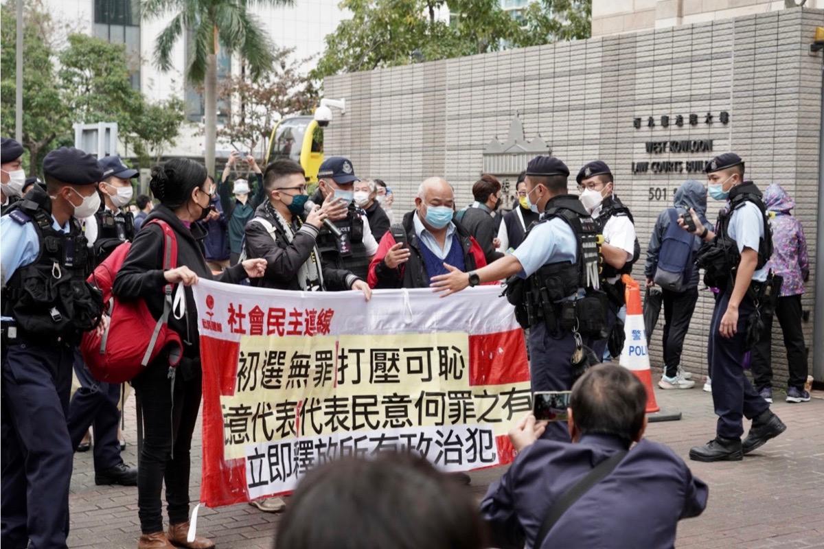 Three members of the "League of Social Democrats" staged a protest outside the trial of the "HK 47", demanding the release of political prisoners. They were surrounded by a large contingent of police officers and taken to the "demonstration area" on the opposite side in Hong Kong's West Kowloon Magistrates' Court on Feb. 6, 2023. (Adrian Yu/The Epoch Times)