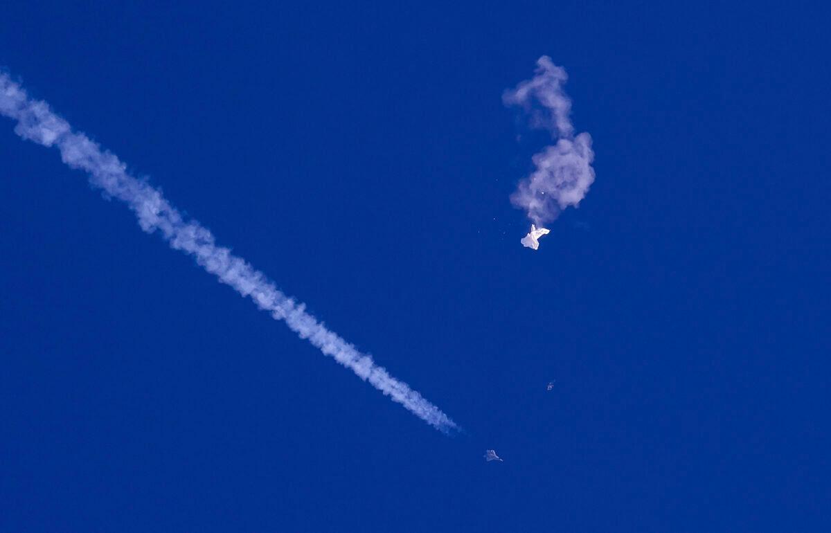The remnants of a large balloon drift above the Atlantic Ocean, just off the coast of South Carolina, with a fighter jet and its contrail seen below it, on Feb. 4, 2023. (Chad Fish via AP)