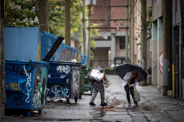A woman prepares to smoke a cigarette in an alley after using illicit drugs at an outdoor supervised consumption site in the Downtown Eastside of Vancouver, on May 27, 2021. (The Canadian Press/Darryl Dyck)