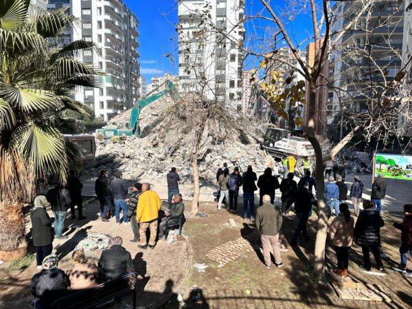 Local residents look on as a crane sifts through the rubble of an eight-floor building that collapsed after the second of two earthquakes in Adana province, Turkey, on Feb. 6, 2023. (Ercan Koc for The Epoch Times)